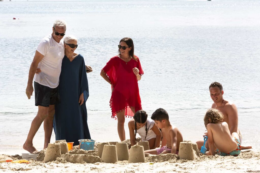 Kids building sandcastles with parents and grandparents on the beach at Windjammer Landing