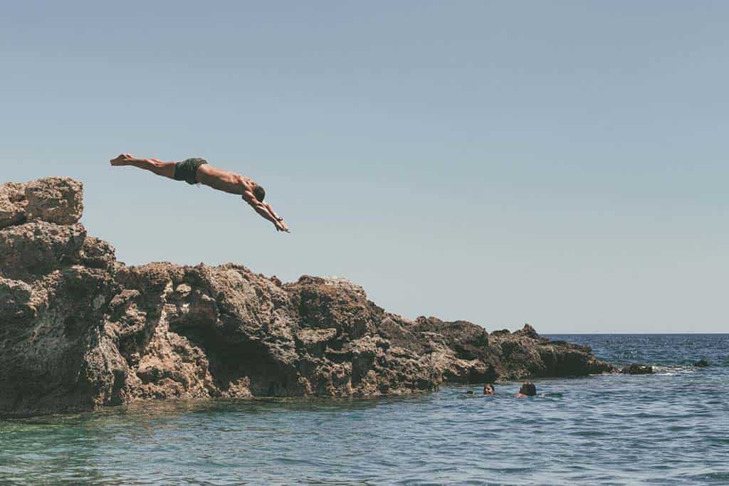 Mann taucht von einem großen Felsen ins Meer auf Kreta, Griechenland