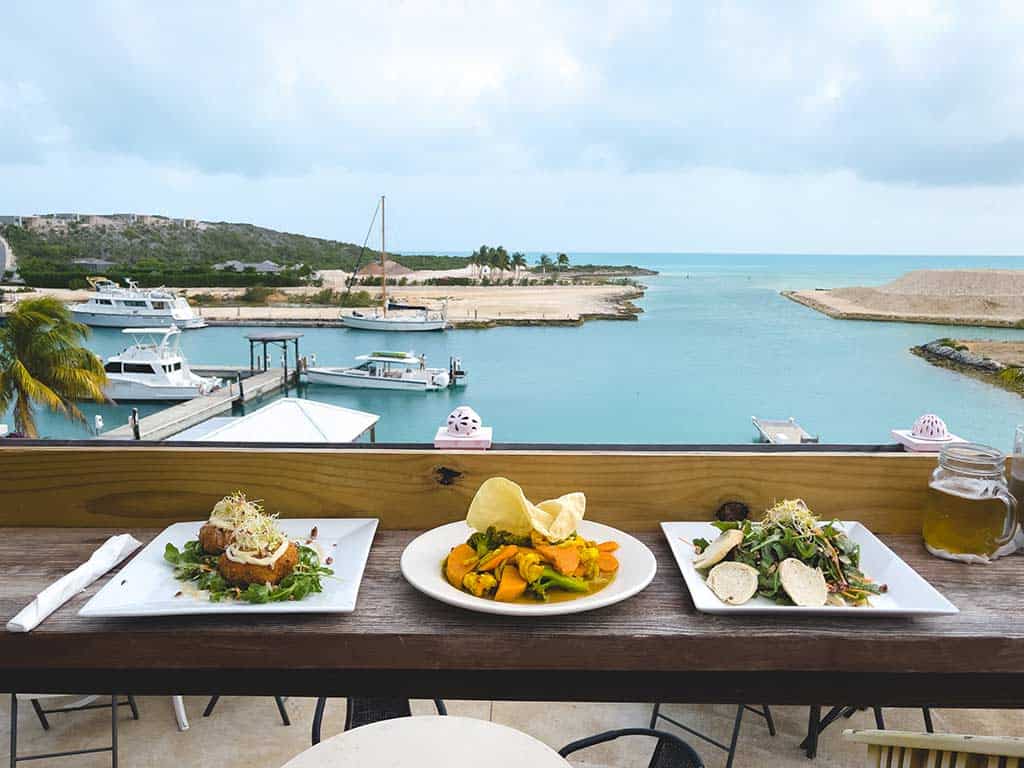 Plated meals set on an outdoor bar overlooking a marina.