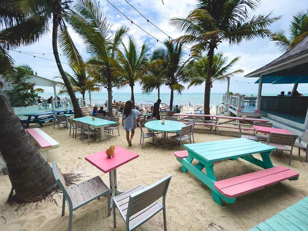 Outdoor tables and chairs set in the sand at an oceanfront restaurant.