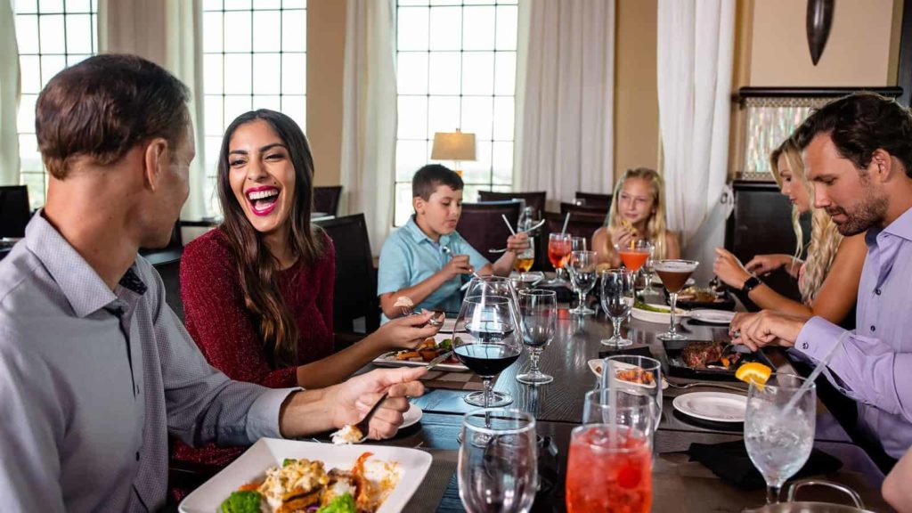 ट्रेडिशन्स रेस्तरां में टेबल पर बात करते और हंसते परिवार।