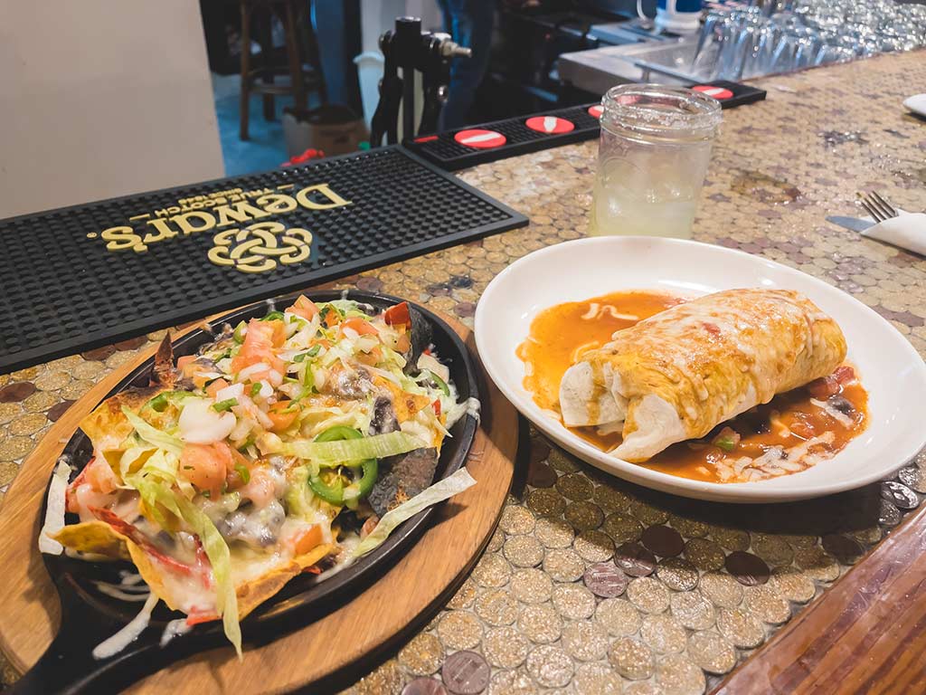 Plated nachos in a cast iron skillet and a burrito set on a bar countertop.