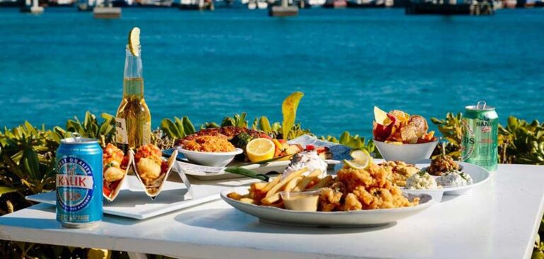 Mesa de restaurante llena de comida y cerveza con vista al mar