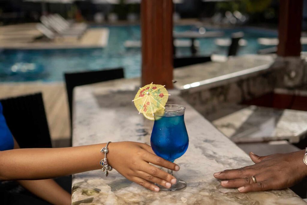 Mano sosteniendo una bebida tropical en el bar junto a la piscina de Cap Cove Resort