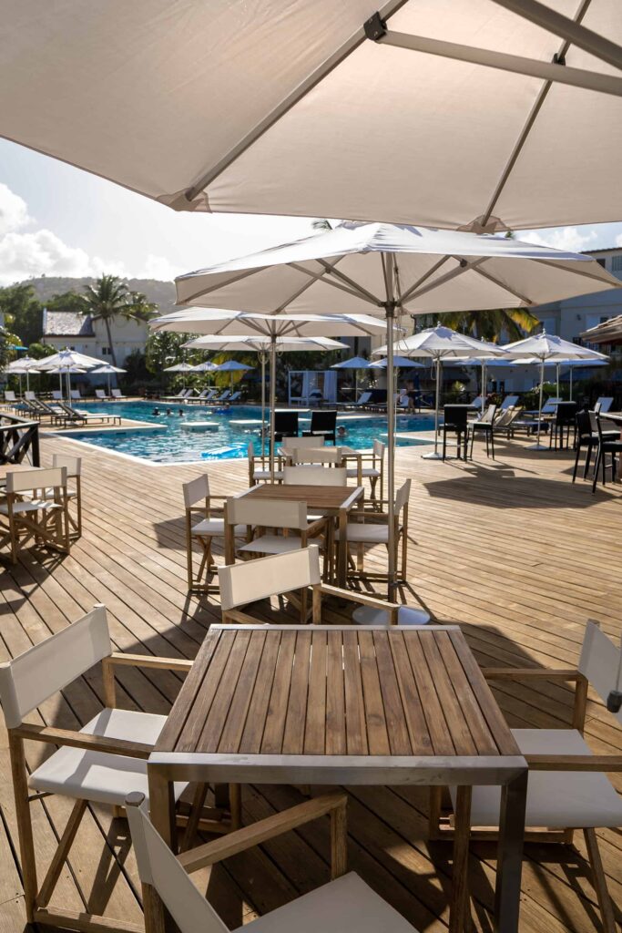 Mesas de comedor junto a la piscina de Cap Cove Resort bajo la sombra de sombrillas