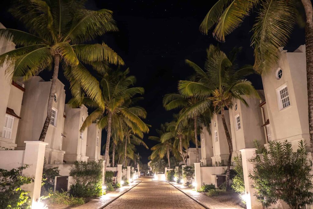 Pasarela de ladrillos de Cap Cove Resort bordeada de villas y palmeras por la noche