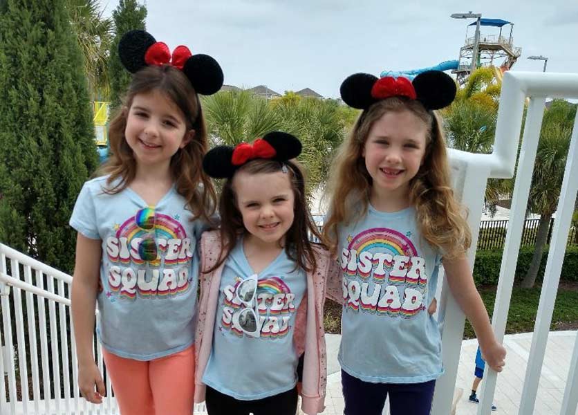ثلاث فتيات صغيرات في قمصان متطابقة يرتدون أذني ميني ماوس