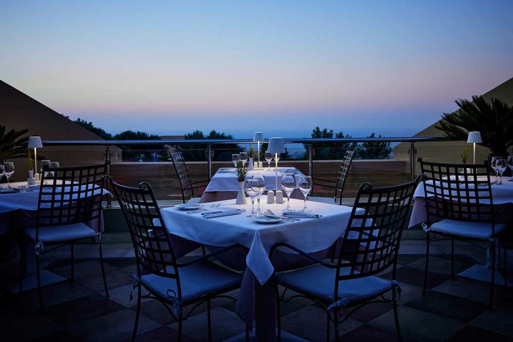 Elegante Tische und Stühle im Freien auf einer Terrasse mit Blick auf das Meer bei Sonnenuntergang