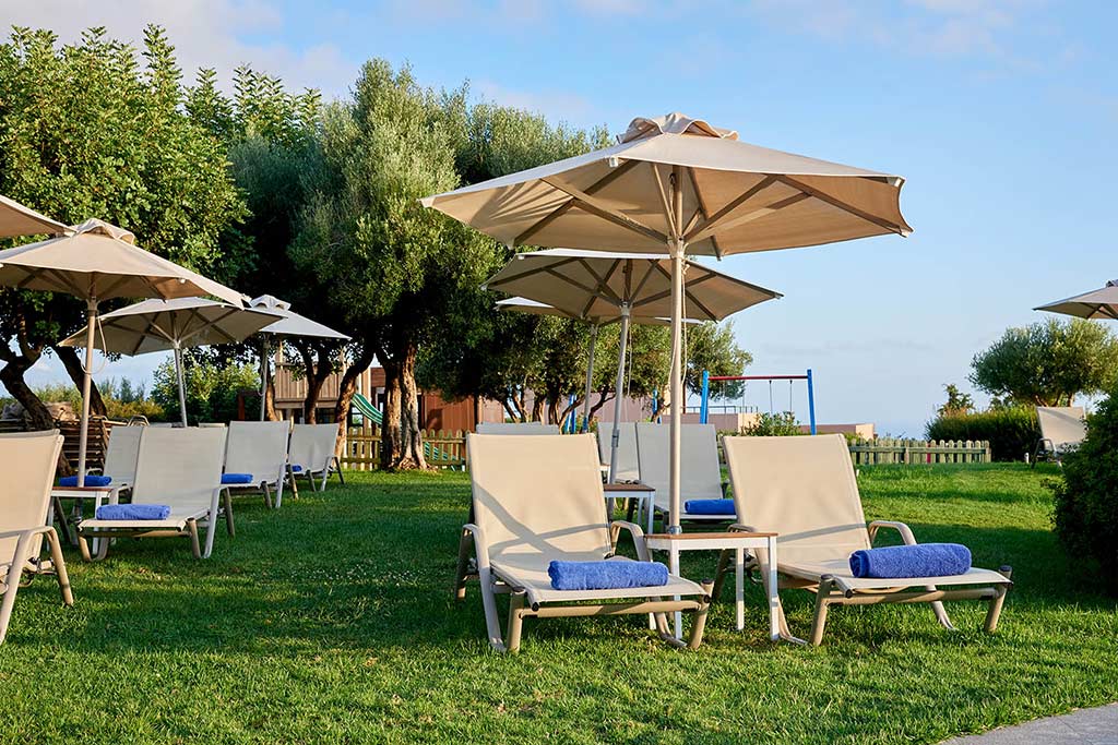 Rows of lounge chairs on grass with folded towels, side tables, and umbrellas