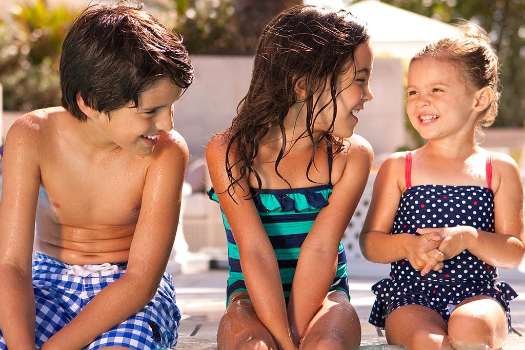 Three kids sitting at the edge of a pool laughing