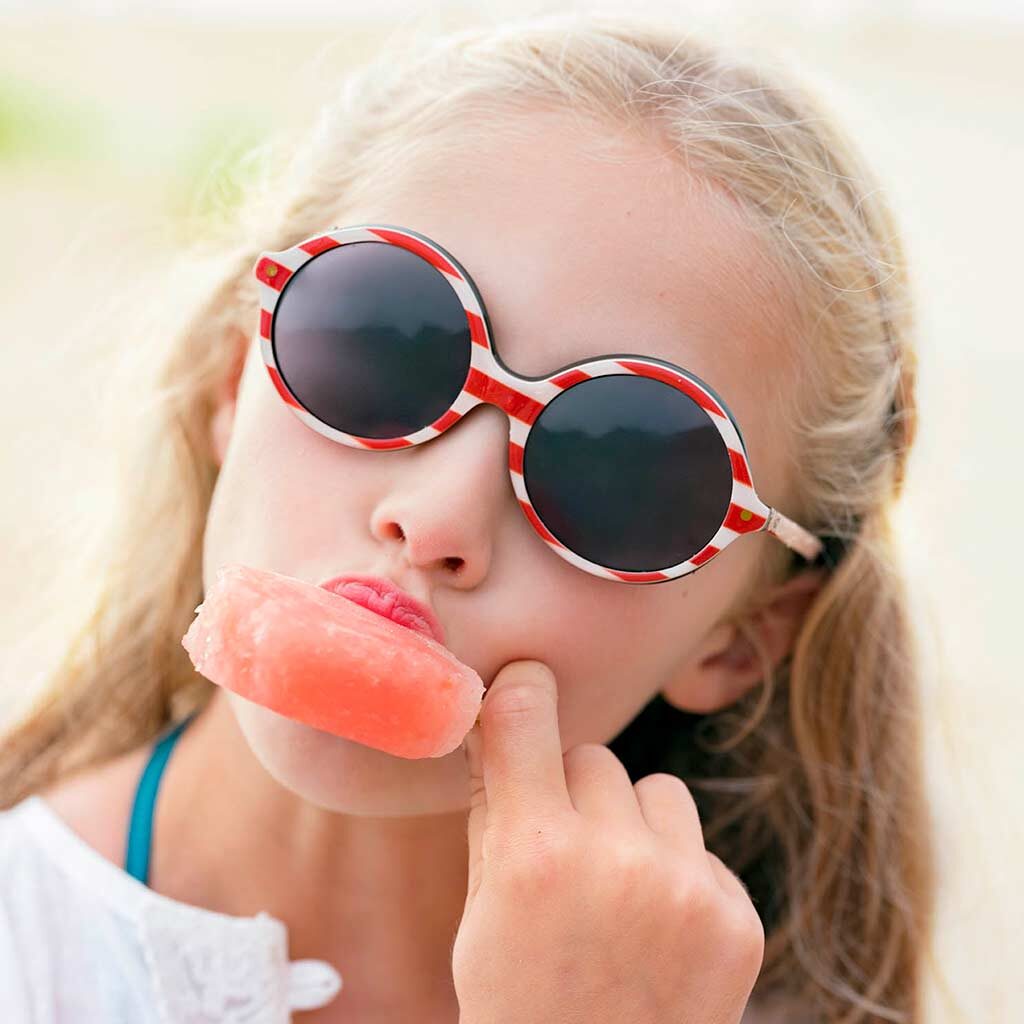 Young girl wearing sunglasses while eating a popsicle