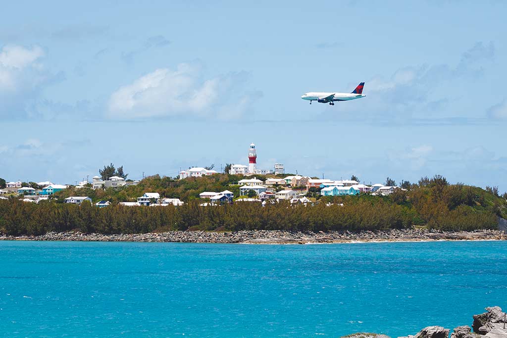 Consejos para viajar cuando vas a las Bermudas en un avión sobrevolando edificios y un faro