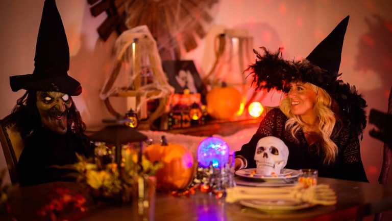 Woman dressed in a witch costume sitting at a table surrounded by spooky halloween decorations