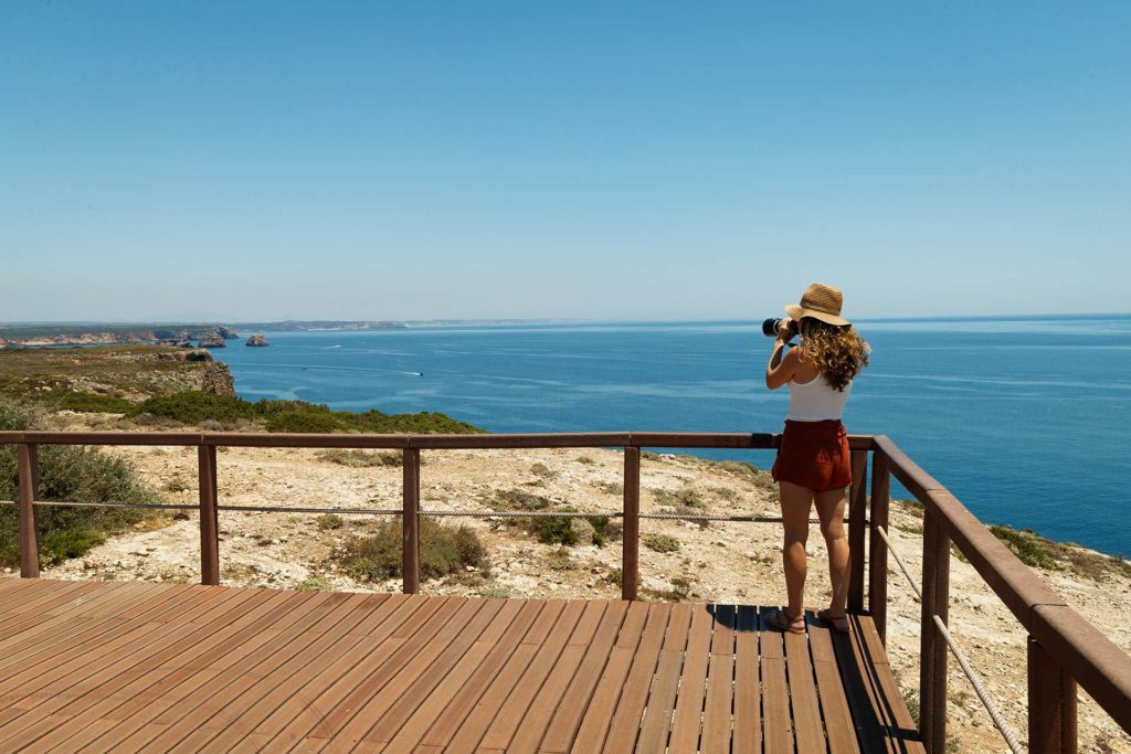 Woman standing on an overlook taking photos of the ocean in Algarve, Portugal