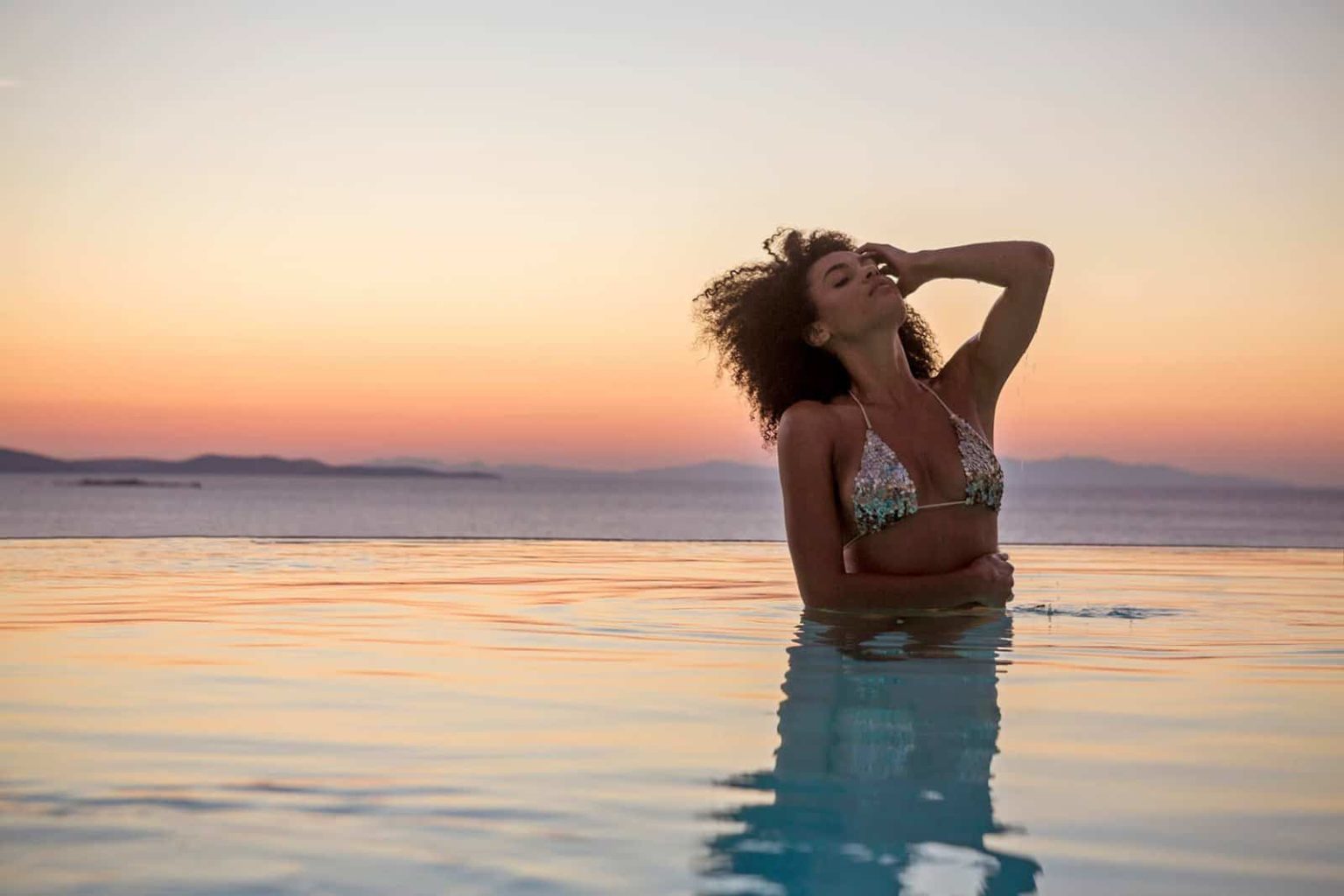 Woman relaxing in a pool at sunset - Boheme Mykonos