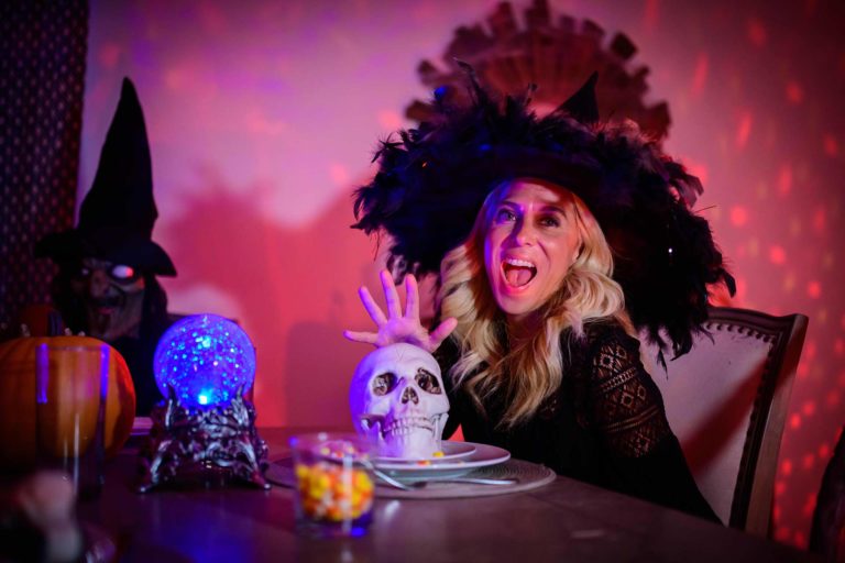 Woman dressed in a witch costume sitting at a table surrounded by spooky halloween decorations