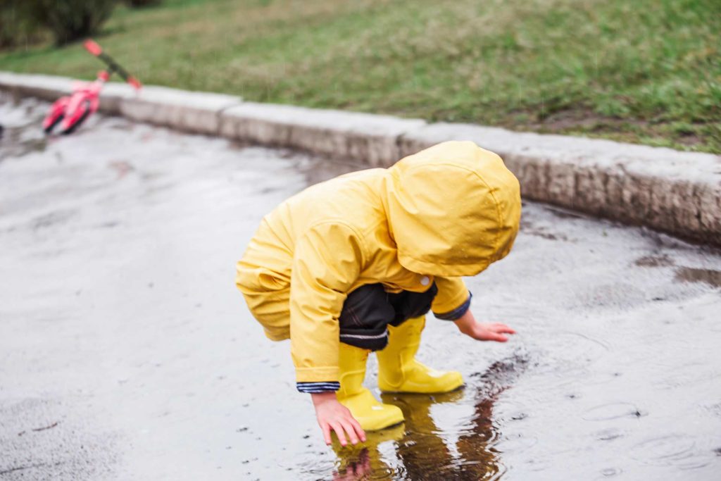 طفل يرتدي معطفًا أصفر من المطر والكالوشات يقفز في بركة مياه
