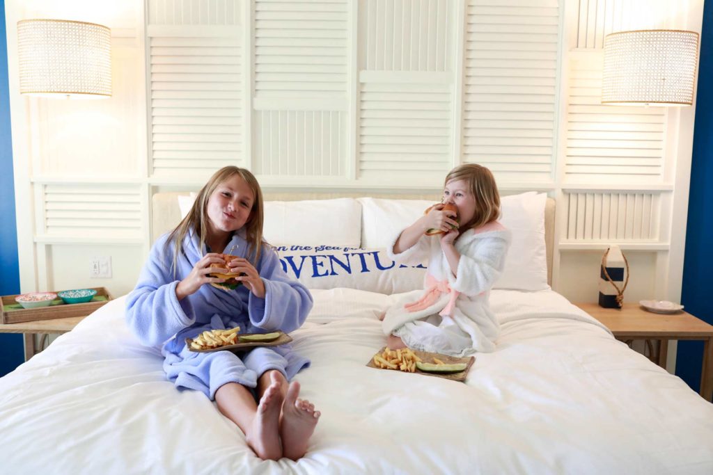 Little girls wearing bathrobes eating burgers in bed