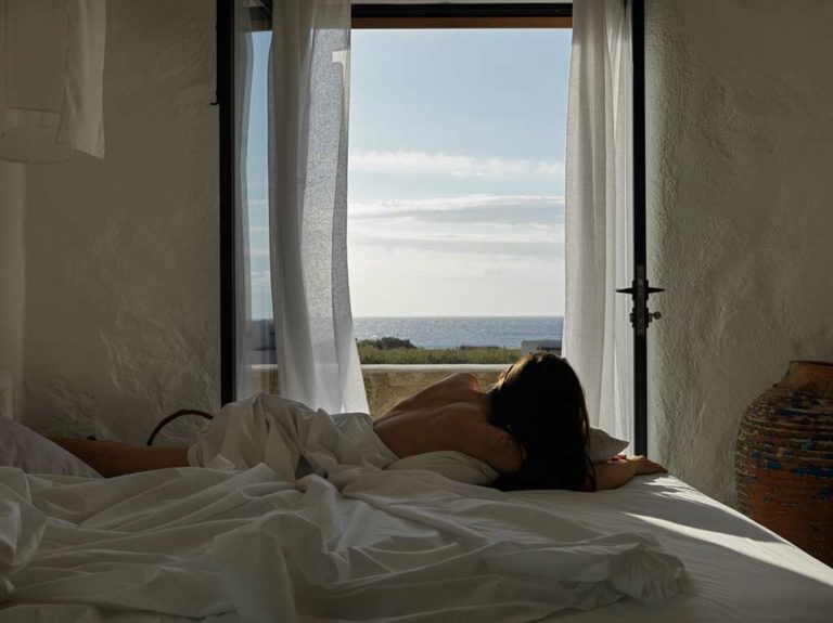 Nomad Mykonos - Mujer acostada en la cama mirando el océano en la suite de luna de miel