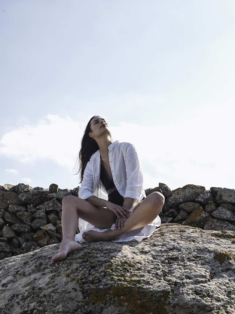Frau, die sich in der Sonne entspannt, während sie auf einem Felsen sitzt