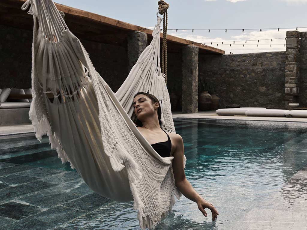 घुमंतू मायकोनोस में एक पूल के ऊपर एक झूला में आराम करती महिला