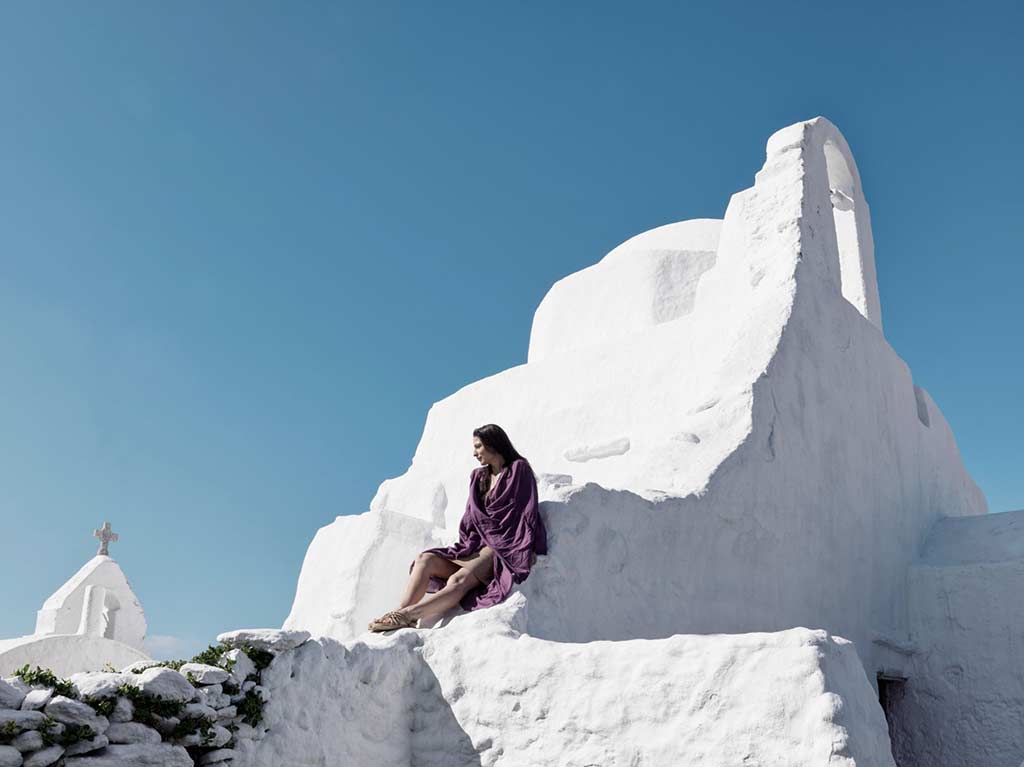 Mujer descansando al lado de un edificio en un pueblo de Mykonos, Grecia