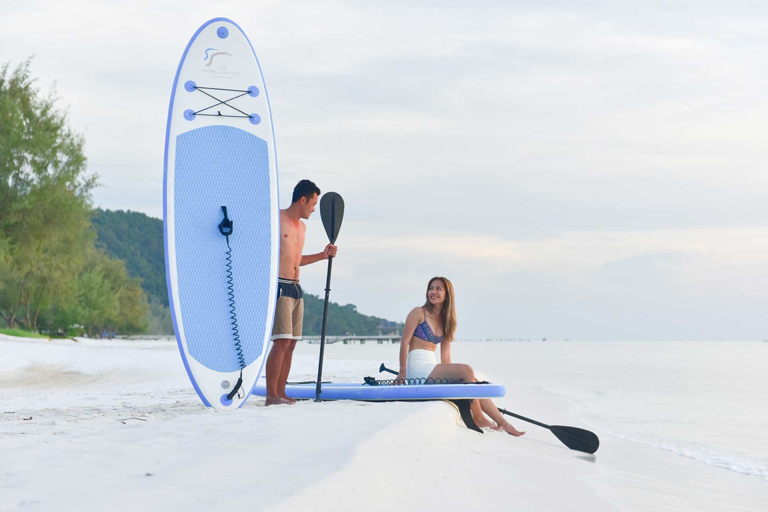 Couple with paddleboard gear sitting on the beach at the Royal Sands Koh Rong