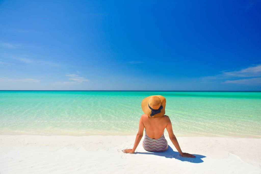 امرأة ترتدي قبعة شمسية تجلس على الشاطئ وتطل على المحيط