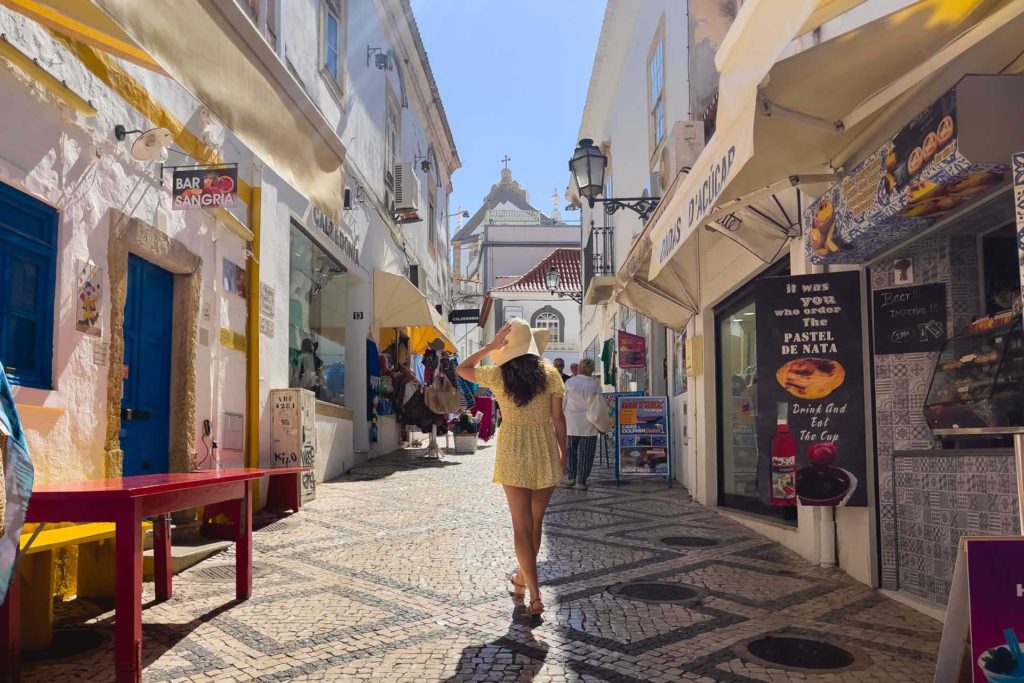 Frau zu Fuß auf einem gepflasterten Weg, gesäumt von Geschäften und Restaurants in der Altstadt von Albufeira, Portugal