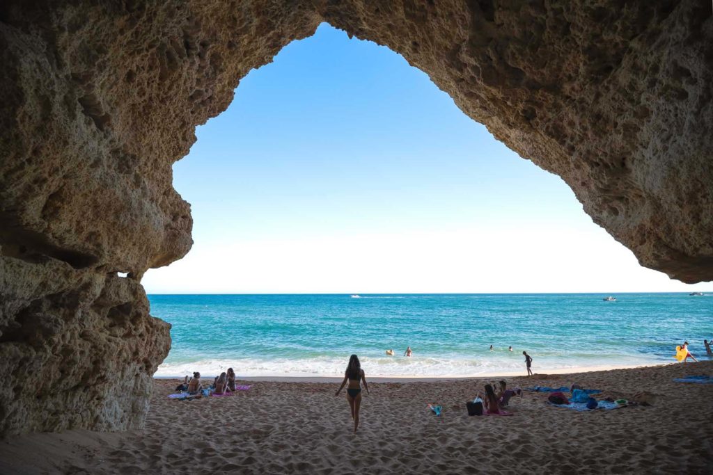 Beachgoers under a seaside cliff cave at the Praia do Castelo beach in Albufeira, Portugal
