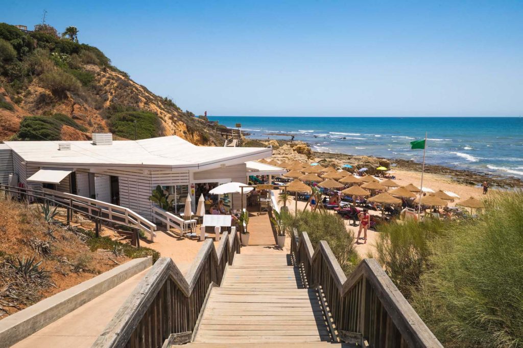 Escalera que conduce a una playa junto al mar bordeada de tumbonas y sombrillas en la Praia da Oura en Albufeira, Portugal