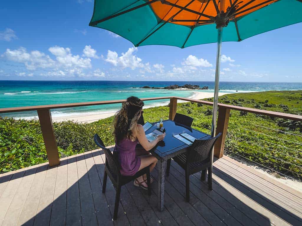 Frau sitzt an einem Tisch auf einer Terrasse mit Blick auf einen Strand in Turks & Caicos