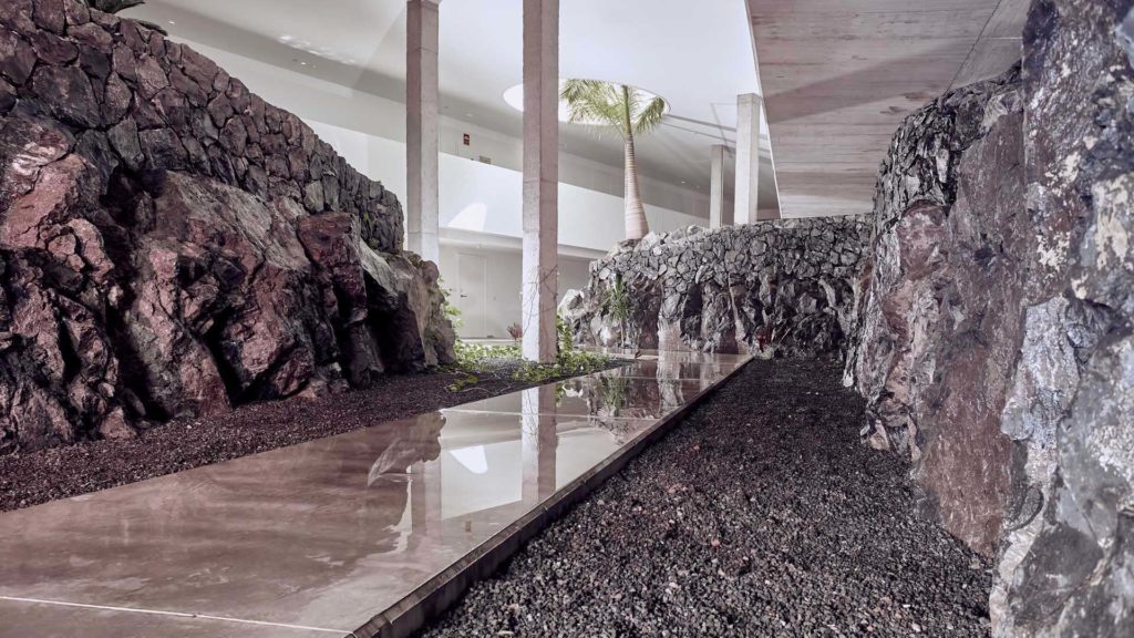 Pasillo al aire libre en el lobby de Baobab Suites rodeado de paredes de piedra natural