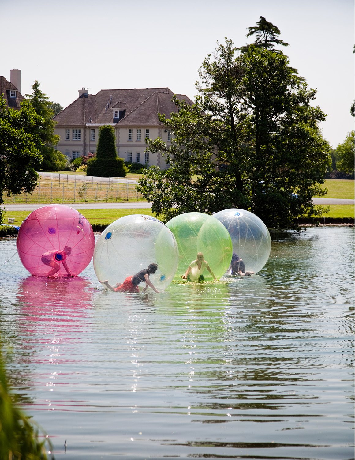 Group of people inside inflatable plastic bubbles on the lake outside of Brockencote Hall