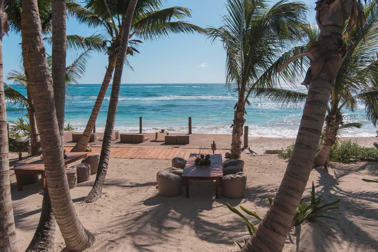 Outdoor tables and chairs in the sand on the beach at Roca Restaurant | Papaya Playa Project