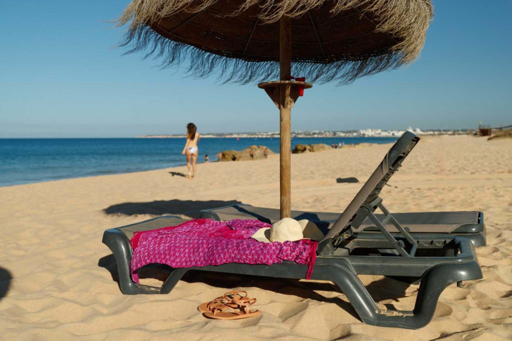 Lounge chair topped with sun clothing under an umbrella at the beach of Salgados Dunas Suites