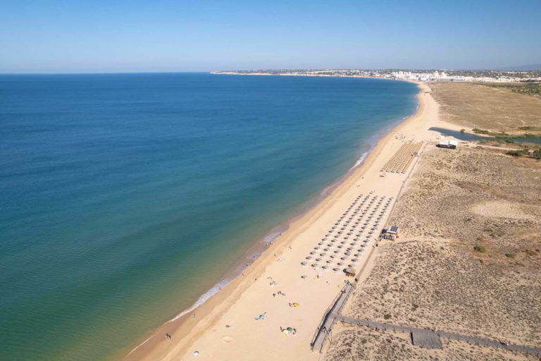 Luftaufnahme des mit Stühlen und Sonnenschirmen gesäumten Strandes der Salgados Dunas Suites