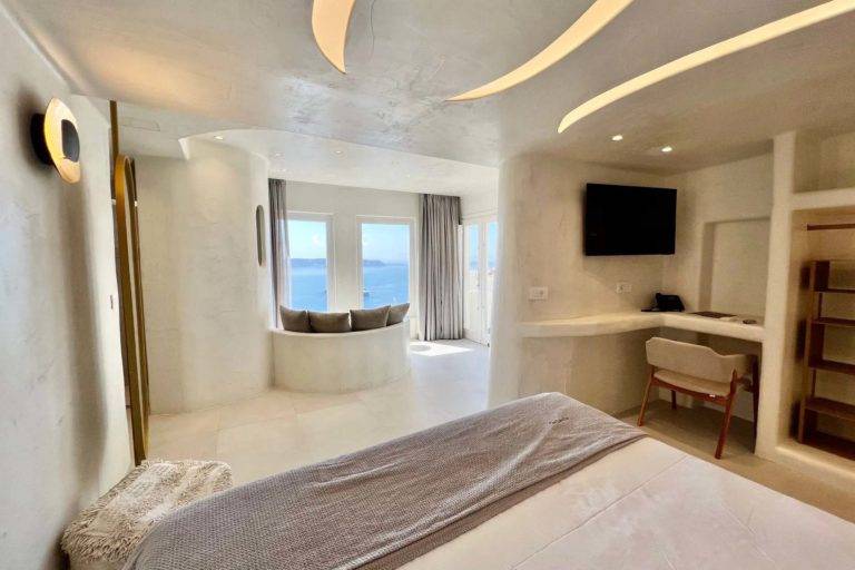 Suite de luna de miel Black Rock: cama, estación de trabajo y sala de estar con vista al mar | Suites de lujo Athina