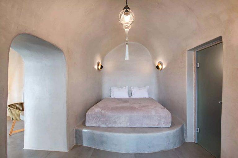 Cave Suite - Área de dormitorio con cama de plataforma, candelabro y candelabros | Suites de lujo Athina