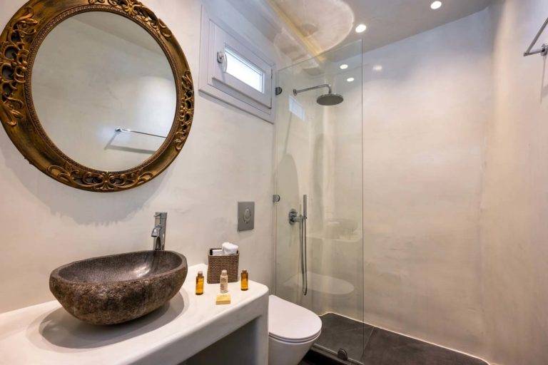 Suite Deluxe - Baño con ducha de lluvia, inodoro, tocador, espejo y artículos de tocador | Suites de lujo Athina