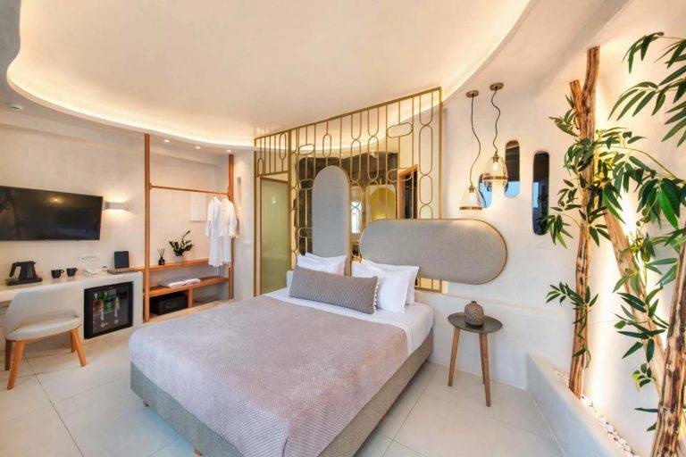 Junior Cave Suite - Dormitorio con cama king size, estación de trabajo, TV, mini refrigerador y armario abierto | Suites de lujo Athina