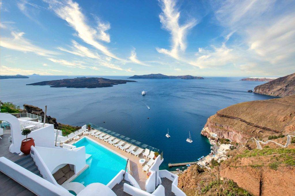 Vista aérea de la piscina y la terraza de la piscina de Athina Luxury Suites rodeadas de vistas de los acantilados y el océano de la isla de Santorini