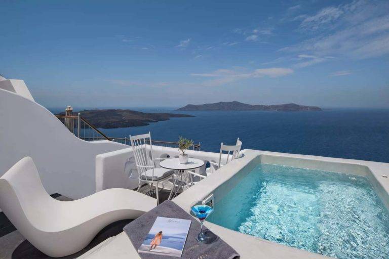 Petit Cave Suite - Balcón al aire libre con mesa de comedor, sillón y jacuzzi con vista al mar | Suites de lujo Athina