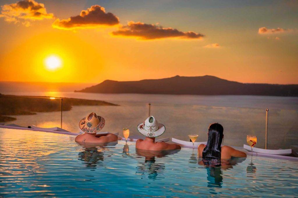 Un pequeño grupo de personas en la piscina infinita de Athina Luxury Suites con cócteles mirando el océano al atardecer