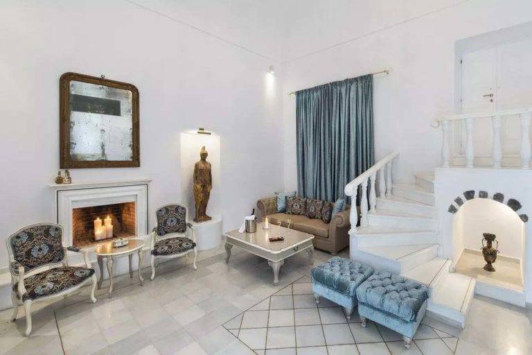 Royal Suite - Sala de estar con sofá, mesa de café, sillones y chimenea a la luz de las velas | Suites de lujo Athina