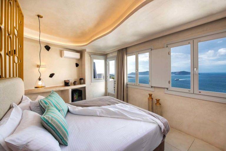 Suite Superior: dormitorio con cama King, ventanas con vista al mar y puerta que conduce al balcón exterior | Suites de lujo Athina