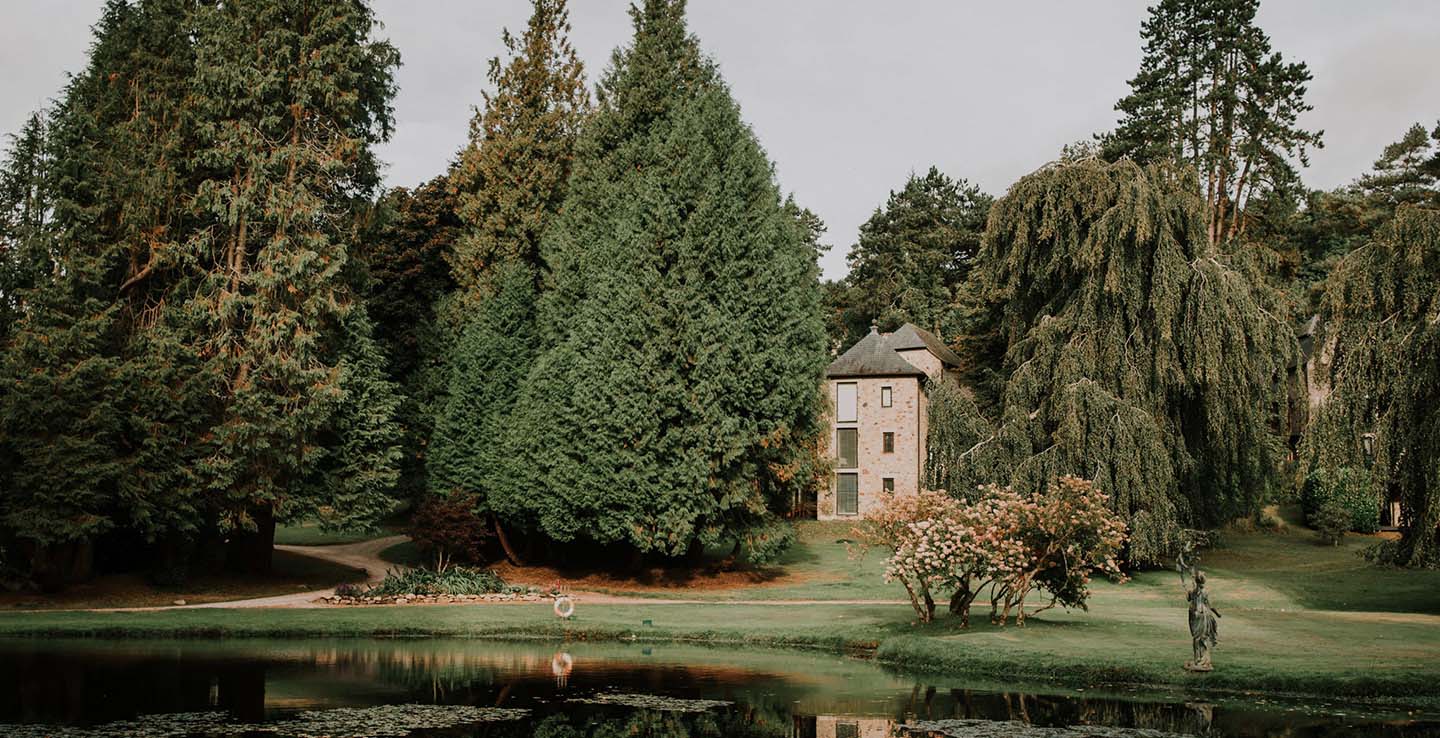 Bovey Castle lodge by a pond, surrounded by greenery
