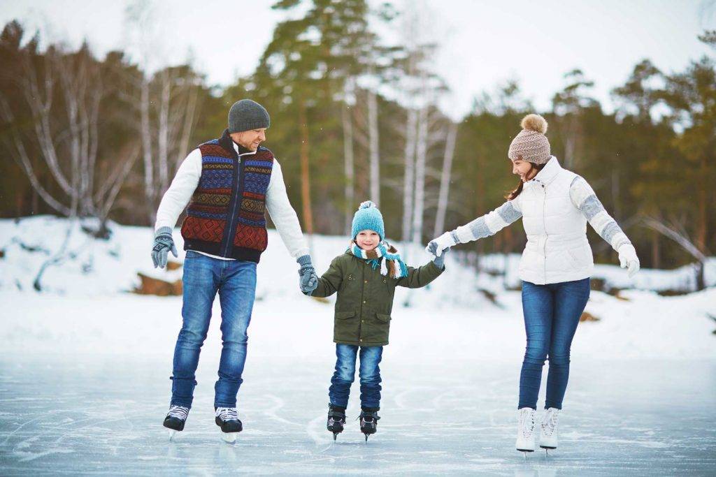 तीन लोगों का परिवार सर्दियों की छुट्टियों में आइस रिंक पर स्केटिंग करता हुआ।