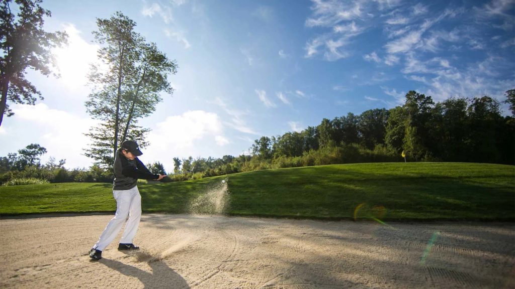 Hombre jugando al golf sacando una pelota de golf de la trampa de arena en el campo de golf Mystic Rock | nemacolina