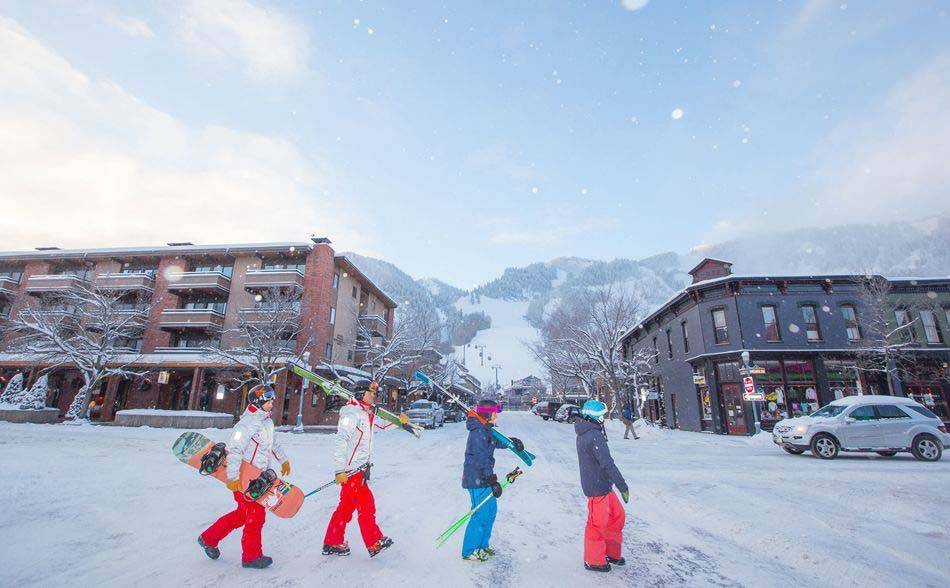 Kleine Gruppe von Menschen mit Ski- und Snowboardausrüstung, die in der Innenstadt von Aspen, Colorado, spazieren